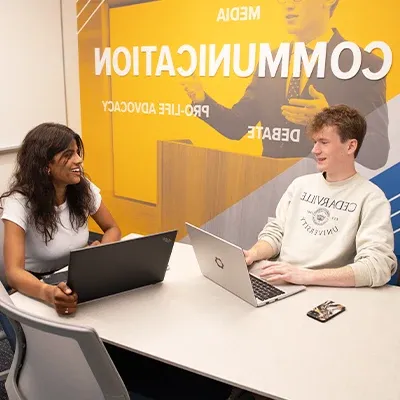 Two students studying with laptops at table.